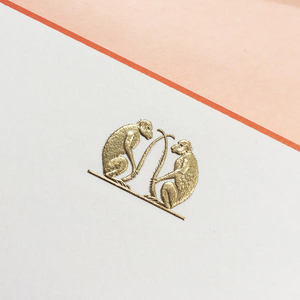 The Printery Monkey Card Set features gold double monkeys facing each other, holding a thin vertical object, on an ecru card with terra cotta borders and a pink background.