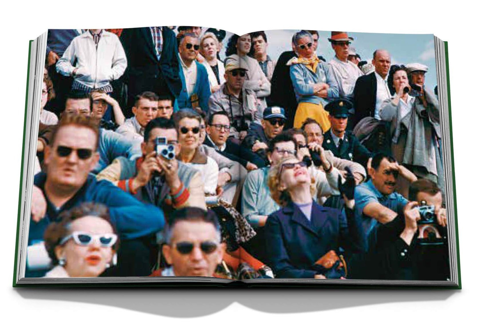 A crowd with cameras and sunglasses are seated outdoors, captivated by an event reminiscent of "The Impossible Collection of Golf" by Assouline.