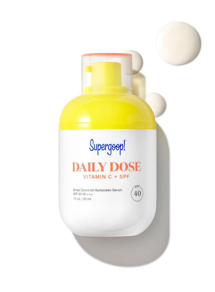 A bottle of Supergoop! Daily Dose Vitamin C + SPF 40 Serum with a pump dispenser, featuring a Brightening Complex and accompanied by an isolated dollop of the product against a white
