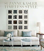 A living room featuring a beige sofa, two round glass tables, and abstract black and white art in square frames exudes the timeless style of Suzanne Kasler. Rizzoli's "Suzanne Kasler: Timeless Style" highlights her haute couture details, showcasing her interior design mastery.