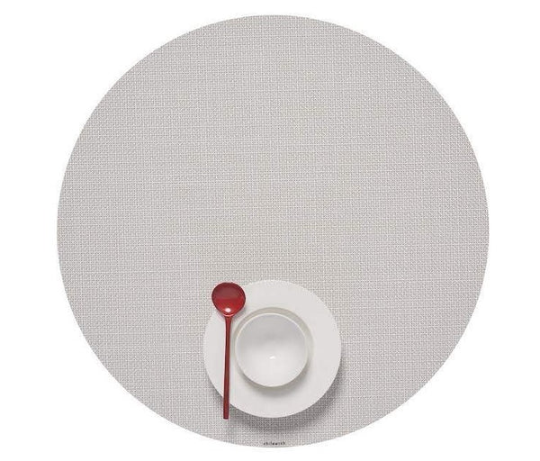 A neatly arranged white bowl and a red spoon set on a Round Placemat in Sandstone made of Chilewich Terrastrand yarns in a Mini Basketweave design.