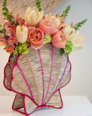 The Shell Flower Vase by Mercedes Salazar, crafted by skilled Bogotá artisans, holds a beautiful arrangement of pink and cream flowers with greenery on a white surface.
