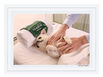 Gray Malin’s “The Pampered Pug” (15.5” x 21”, white frame) captures a small white dog being gently massaged on a table at the Beverly Hills Hotel, with a rolled towel near its head.