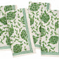 Four folded white cloth napkins from the Pomegranate Inc. Dancing Artichokes Collection, featuring a green and white print of hand-painted globe artichokes and leaf patterns, are arranged in a staggered layout.
