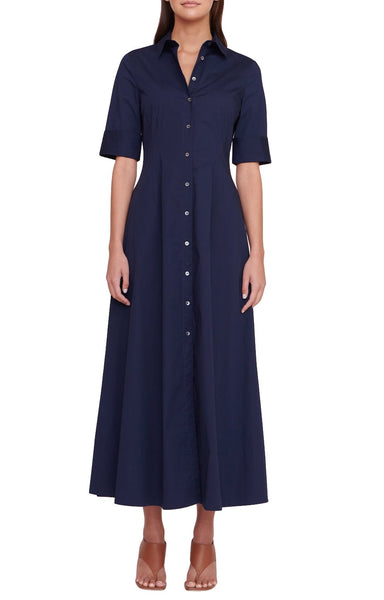 A woman wearing a Staud Joan Maxi Dress in dark blue with short sleeves and a row of buttons down the front, paired with tan sandals.