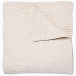 A folded cream-colored quilt from the Vivada Bedding Collection by John Robshaw features a hand-stitched, textured grid pattern with one corner flipped over to reveal its reversible design, beautifully capturing the timeless appeal of classic quilts.