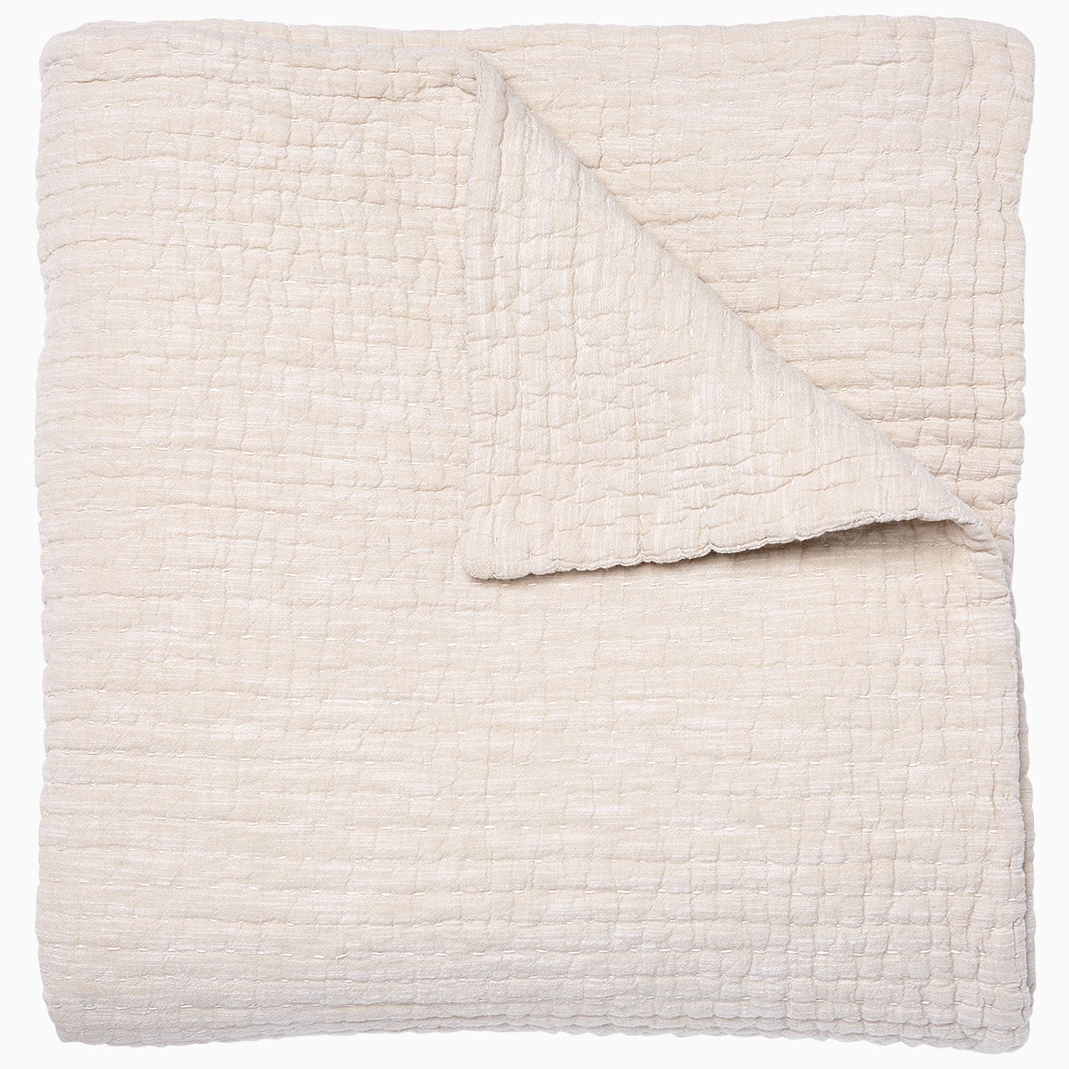 A folded cream-colored quilt from the Vivada Bedding Collection by John Robshaw features a hand-stitched, textured grid pattern with one corner flipped over to reveal its reversible design, beautifully capturing the timeless appeal of classic quilts.