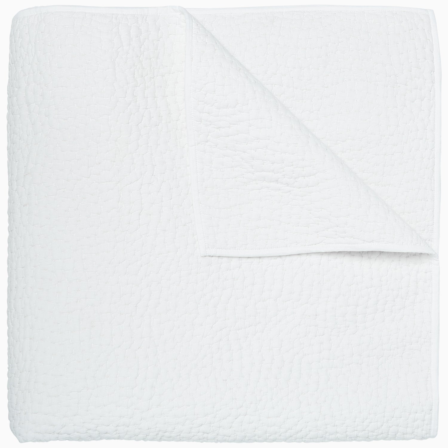A neatly folded white coverlet from the John Robshaw Hand-Stitched Bedding Collection, featuring a textured pattern and shown from above with one corner turned down to reveal the underside. Crafted from soft cotton voile, this piece blends comfort and elegance.