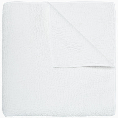 A neatly folded white coverlet from the John Robshaw Hand-Stitched Bedding Collection, featuring a textured pattern and shown from above with one corner turned down to reveal the underside. Crafted from soft cotton voile, this piece blends comfort and elegance.