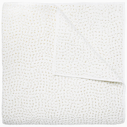 A white coverlet from the Hand-Stitched Bedding Collection by John Robshaw, featuring a subtle stitched pattern and organic cotton, is neatly folded with one corner turned down to reveal its detailed texture.
