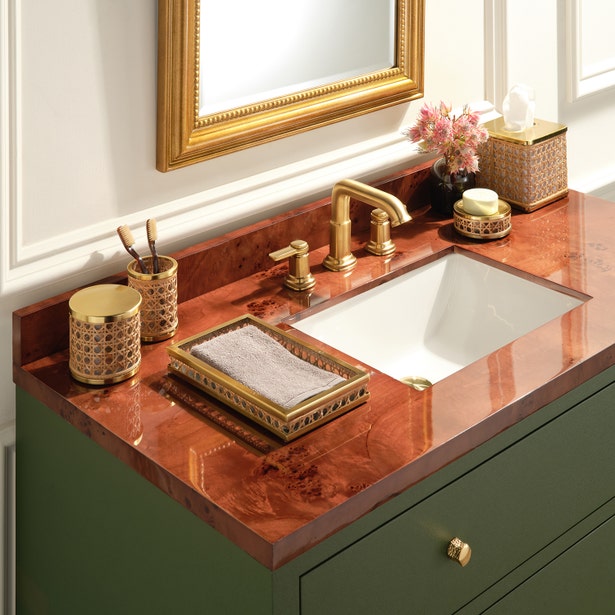 The Norwell Bath Collection by Pigeon & Poodle showcases a bathroom vanity with a red marble countertop, gold faucet and accessories, rectangular sink, folded towel, décor pieces, and a framed mirror.