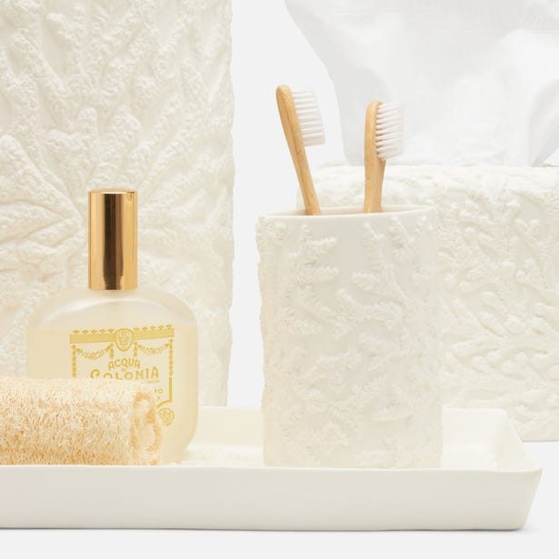 The Alanya White Bath Collection by Pigeon & Poodle includes elegant white porcelain accessories with a coral-like texture: tissue box, soap bottle, loofah, and toothbrush holder with two bamboo toothbrushes, all on a sleek tray.