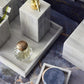 The Arles Bath Collection by Pigeon & Poodle features a sleek marble tray that stylishly displays a gold soap dispenser, glass jar, two toothbrushes, and a round coaster, elevating your bathroom on any dark marble countertop.