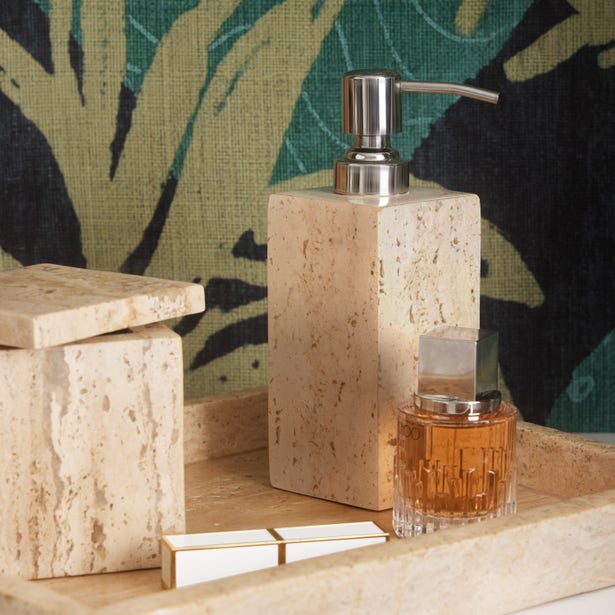 A stone soap dispenser, lidded container, glass perfume bottle, and rectangular box from Pigeon & Poodle's Bowen Natural Bath Collection sit on a stone tray against a leafy patterned background.