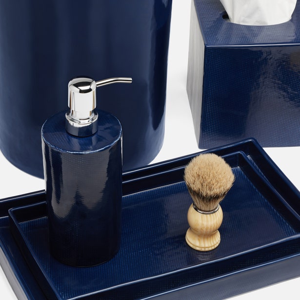 A soap dispenser, shaving brush with wooden handle, and tissue box from Pigeon & Poodle’s Cordoba Navy Bath Collection are arranged on matching hand-textured navy trays.
