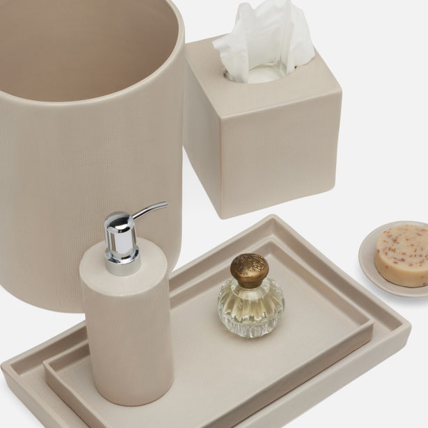 The Cordoba Bath Collection by Pigeon & Poodle features beige ceramic bathroom accessories with a burlap texture and hand-textured finish, including a waste bin, tissue box, soap dispenser, trays, and glass bottle—displayed on white.