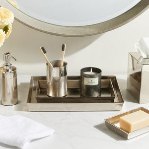 A shiny nickel tray from the Hagen Bath Collection by Pigeon & Poodle holds two toothbrushes, a metal cup, candle, and soap dispenser. A matching soap dish, tissue box, towel, and flower vase complete this elegant countertop display.
