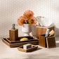The Harper Dark Teak collection by Pigeon & Poodle features a soap dispenser, trays, tissue box, toothbrush holder, and vase with orange flowers on a bathroom countertop against a hexagon tile wall—elegant details complete the look.