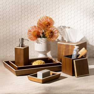 The Harper Dark Teak collection by Pigeon & Poodle features a soap dispenser, trays, tissue box, toothbrush holder, and vase with orange flowers on a bathroom countertop against a hexagon tile wall—elegant details complete the look.