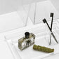 A clear tray from the Monette Bath Collection by Pigeon & Poodle holds a rectangular perfume bottle with a black cap, a bundle of sage, and a clear holder containing two black toothbrushes.