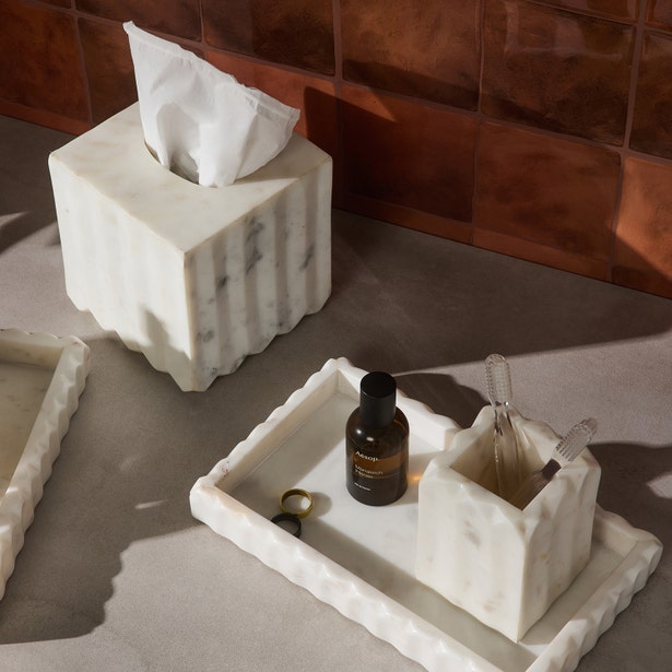 The Proviso White Bath Collection by Pigeon & Poodle features a pleated marble tissue box, tray, toothbrush holder, and ring—styled on a gray counter with a brown tile backdrop—ideal for luxury home decor.
