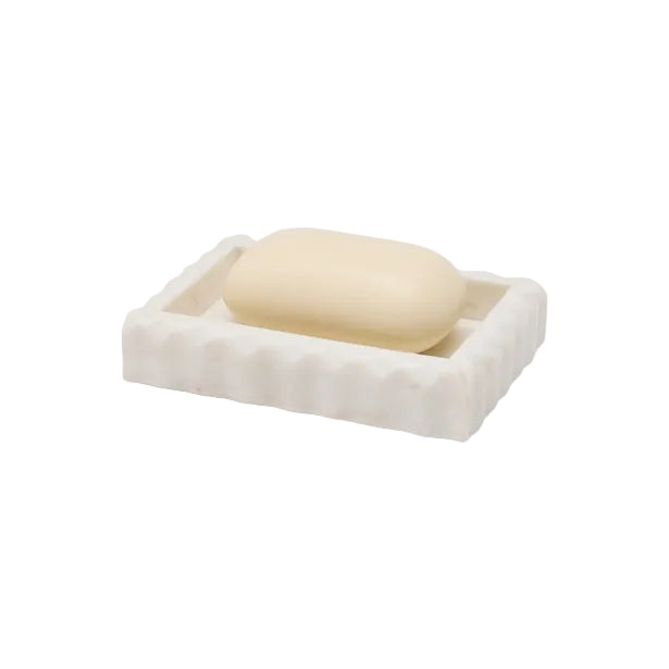 A bar of soap sits on a rectangular white soap dish with raised edges and subtle pleated marble details from Pigeon & Poodle’s Proviso White Bath Collection—an elegant accent for luxury home decor.