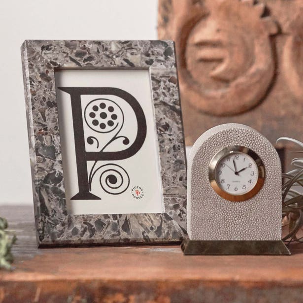 A decorative letter "P" in a Pigeon & Poodle Corsica Frame Collection frame is displayed beside a small, round-faced clock on a wooden surface.