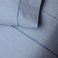 Close-up of a Light Indigo and white patterned organic sheet set from the Cinde Bedding Collection by John Robshaw, featuring small repeating leaf-like shapes in the signature Cinde print, with visible stitching detail.