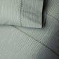 Close-up of a pillow and quilt from the John Robshaw Nandi Bedding Collection, featuring green and white vertical stripes with visible decorative stitching, hand quilted in soft cotton voile.
