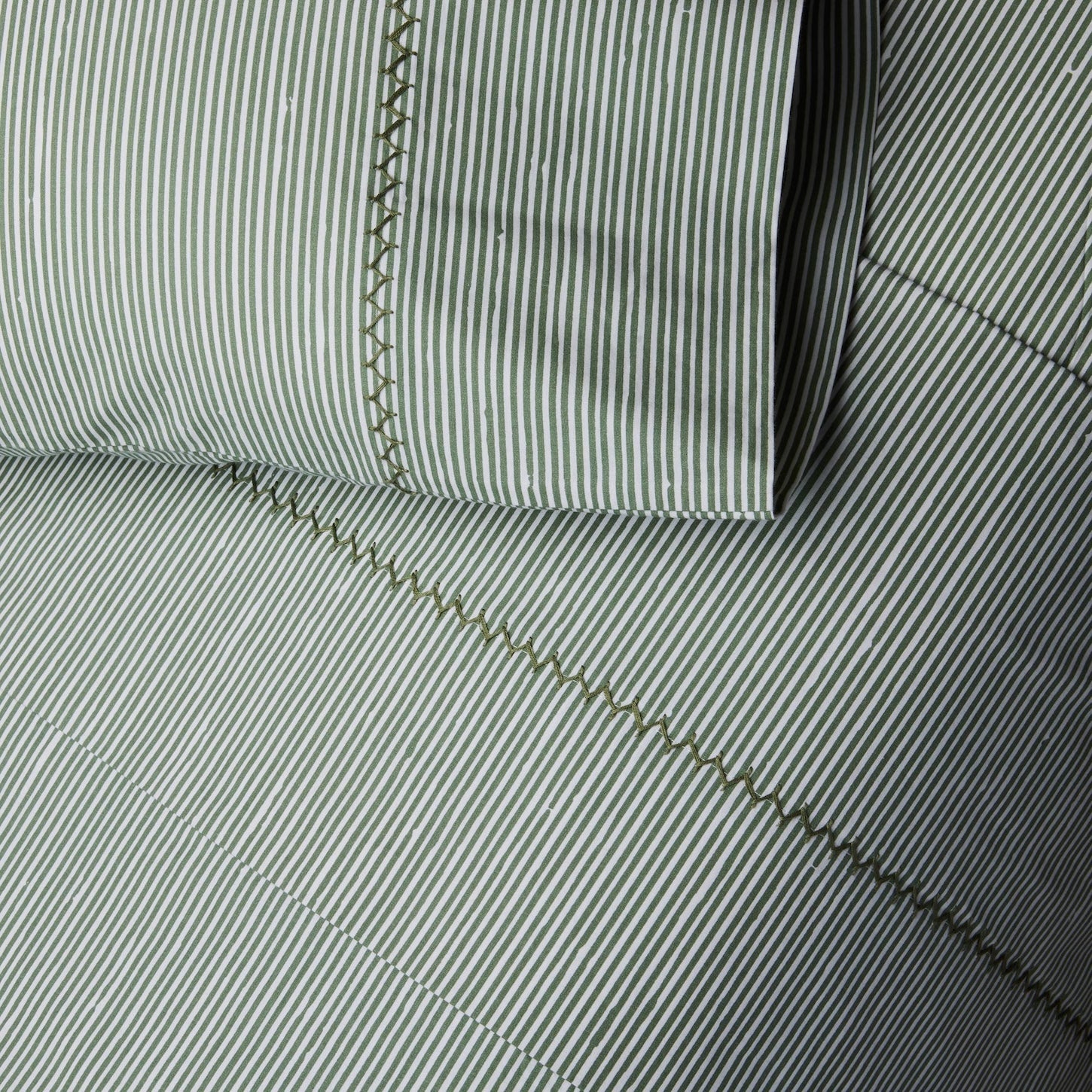 Close-up of a pillow and quilt from the John Robshaw Nandi Bedding Collection, featuring green and white vertical stripes with visible decorative stitching, hand quilted in soft cotton voile.