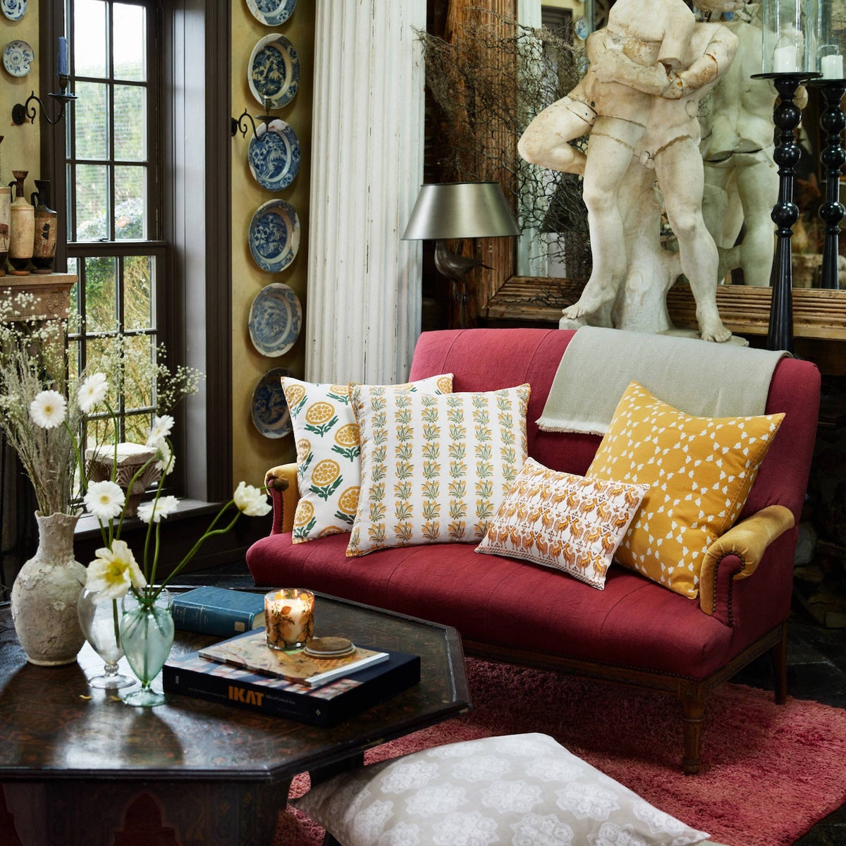 Red loveseat featuring four Yukti Pillow decorative pillows with hand block printed botanical and geometric patterns.
