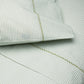 Close-up of a bed featuring the John Robshaw Cinde Bedding Collection, with green and white patterned sheets and pillowcases adorned with a small leaf motif and a decorative green stitched border. This organic sheet set also highlights the delicate Cinde print details for an added touch of style.