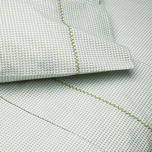 Close-up of a bed featuring the John Robshaw Cinde Bedding Collection, with green and white patterned sheets and pillowcases adorned with a small leaf motif and a decorative green stitched border. This organic sheet set also highlights the delicate Cinde print details for an added touch of style.