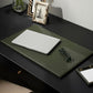 A functional olive green full-grain leather Grafton Laptop Desk Blotter Set from Pigeon & Poodle on a black desk, holding a closed silver laptop and a pair of reading glasses.