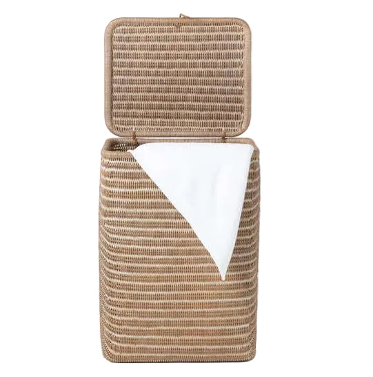 The Mocha Whitewashed Lorain Hamper by Pigeon & Poodle features horizontal rattan weaving, an open lid, and a white towel draped over the edge, all set against a plain white background.