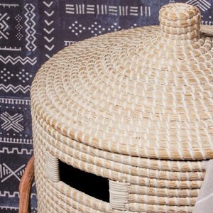 The Pigeon & Poodle Roslyn Hamper in whitewashed seagrass features a lid and cut-out handle, shown against a black and white patterned textile—ideal for stylish storage.