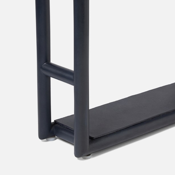 Close-up of the lower section of a modern, dark-finished Bolzano Towel Rack from Pigeon & Poodle, featuring tubular legs and a flat base shelf, offering subtle coastal charm against a white background.
