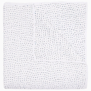 A folded white coverlet from the John Robshaw Hand-Stitched Bedding Collection, featuring small, evenly spaced black stitches in a wavy pattern across soft cotton voile fabric.