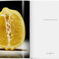 On the left page of "The Gourmand's Lemon: A Collection of Stories and Recipes" by Taschen, a halved lemon spotlights its unique food-art fusion; the right presents a brief dedication on a plain white background.
