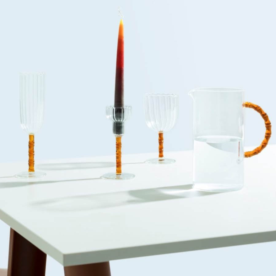 The Rivoli Drinkware and Tealight Collection by Ichendorf Milano features hand-crafted glassware, each piece with a textured orange handle or stem—elegant on any white table.