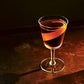 A stemmed glass filled with The Martini by Chronicle Books, beautifully garnished with a twist of orange peel, rests elegantly on a dark surface—a presentation any cocktail expert like Alice Lascelles would appreciate.