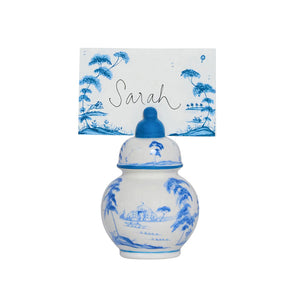 A small blue and white decorative porcelain jar elegantly holds a Juliska Country Estate Place Card with the name "Sarah," featuring a charming country estate motif in its blue landscape design.