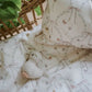 A woven basket holds the Gooselings Bows & Butterfly Kisses Toddler Duvet, featuring floral and ribbon patterns, with a lightweight cover and a small crocheted animal toy resting on top.