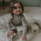 A young child with wavy brown hair plays with illustrated cardboard blocks beside the Gooselings Animal Parade Ivory Toddler Duvet, resting on a patterned blanket in a softly lit room.