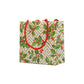 The Caspari Holly and Fretwork White Collection gift bag features a geometric gold-and-white background with green leaves, red berries, and red twisted rope handles—ideal for pairing with festive paper plates or dinnerware.