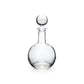 The Benson Drinkware Collection by Simon Pearce features a clear glass decanter with a round stopper and clean-lined Bauhaus-inspired design, elegantly photographed against a white background.