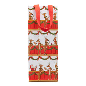 The Caspari Santa Bar Bottle Bag is a festive, heavy-duty paper gift bag with red handles, featuring a unique design of reindeer and Santa Claus at a garland-adorned bar.