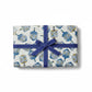 A rectangular gift from Caspari’s Patterned Dreidel Collection, wrapped in white paper adorned with a blue and gold dreidel design and finished with a blue ribbon and bow, makes the perfect Hanukkah holiday present, shown on a white background for a festive touch.