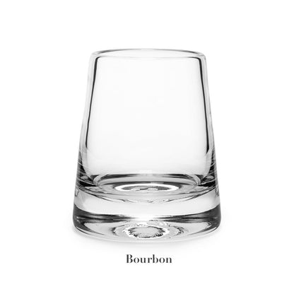 A clear, empty glass labeled "Bourbon" from the Simon Pearce Ascutney Drinkware Collection sits on a white background—an elegant piece of handmade barware.