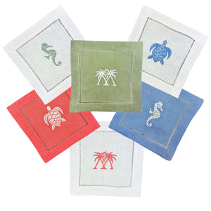 The Coastal Cocktail Napkin Set by Pink House Mustique includes six embroidered linen napkins with colorful coastal designs—turtles, seahorses, and palm trees—for a tropical touch.
